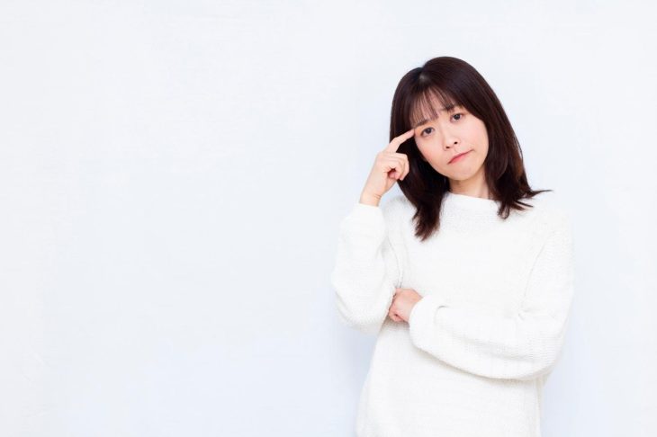 こめかみに指を当て、腕を組む女性