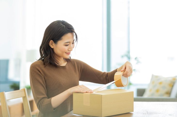 ガムテープで段ボール箱に封をする女性
