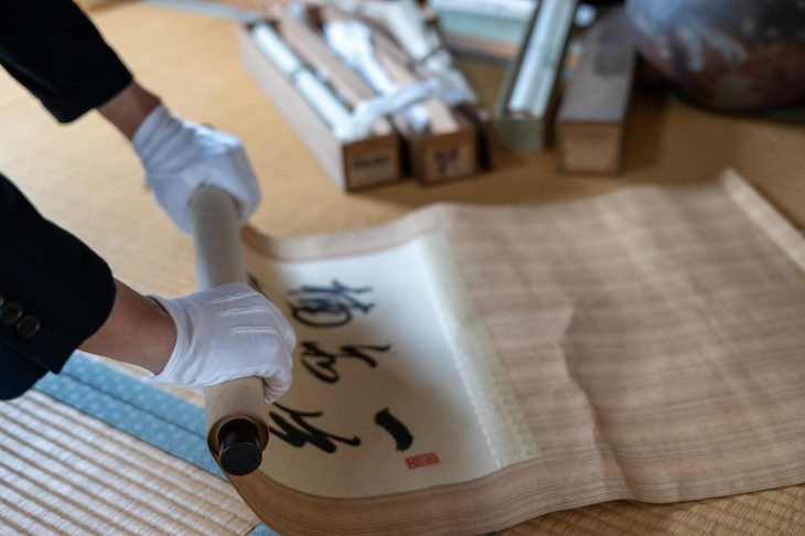 白い手袋をはめて掛け軸を巻き取る手元
