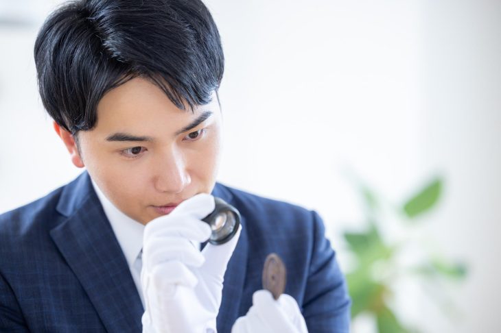 ルーペを使用して古銭を査定する男性