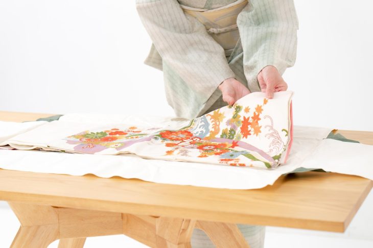 着物姿の女性が、色鮮やかな花柄の着物を丁寧にたたんでいる様子