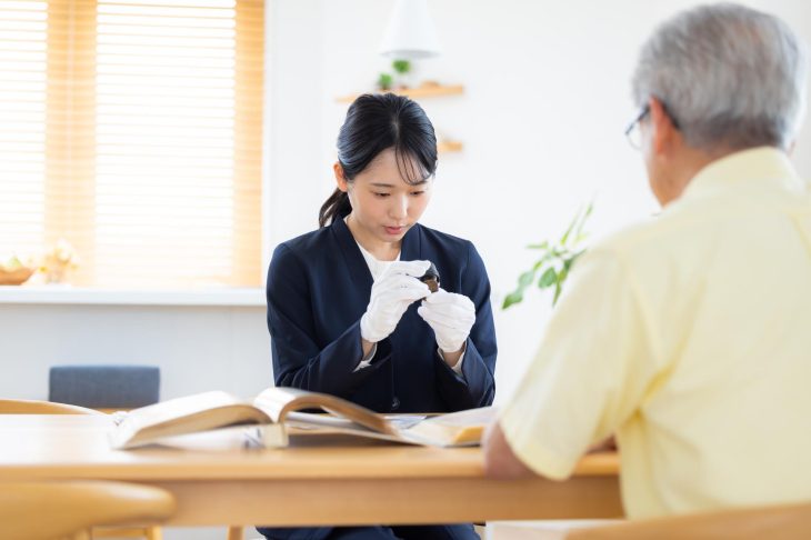 白い手袋をはめてルーペを持ち、訪問査定をしている女性査定士