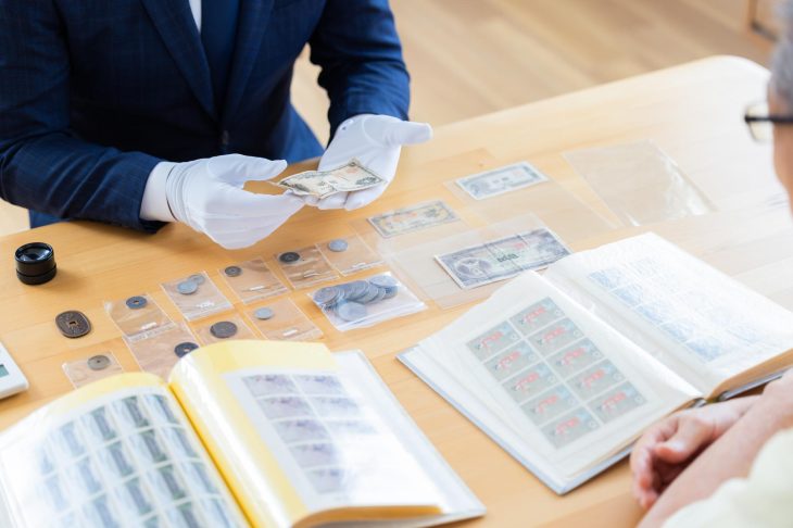 硬貨や古紙幣、切手などをテーブルに並べ、査定士が品物を確認している様子