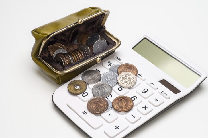 硬貨の入ったがま口財布と、10円玉などの硬貨が置かれた電卓