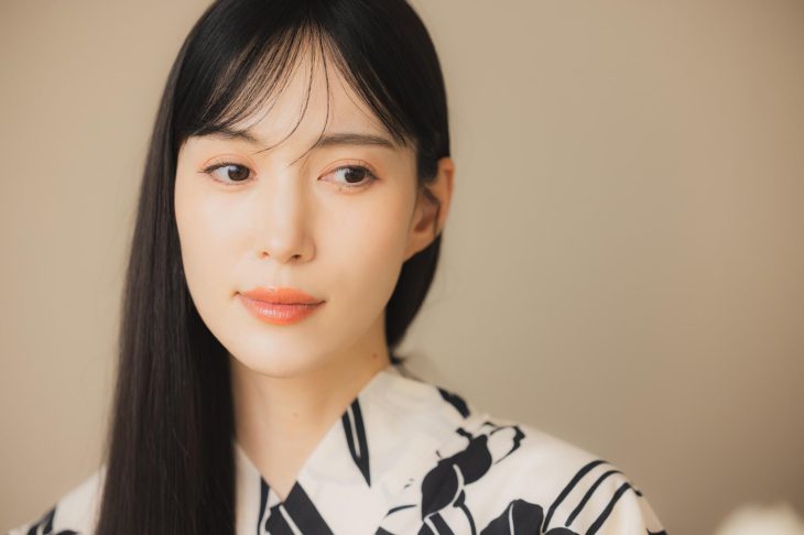 白地に黒の柄が入った着物を着て、ナチュラルなメイクをした女性の顔のアップ