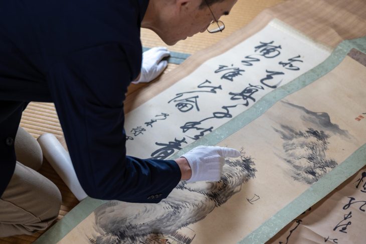 白い手袋をはめて掛け軸を査定する男性